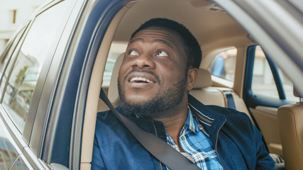 Wall Mural - Traveling Young Man Rides on a Passenger Seat of a Car, Opens Window and Looks on a Big City in Wonder.