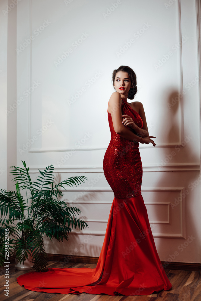 Glamorous brunette woman wearing a red dress standing poses in studio Stock  Photo | Adobe Stock