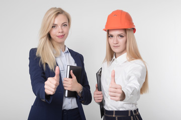 Two beautiful girls construction engineers show finger up on white background