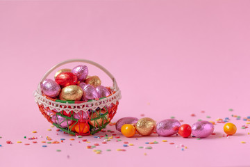 Wall Mural - Sweet Easter candy eggs in basket on pink background.