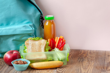 Lunch box with appetizing food and backpack on wooden table.