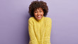 © wayhome.studio  - Horizontal shot of attractive dark skinned female has sincere smile, feels optimistic and glad, being in good mood, dressed in yellow jumper, poses against lilac studio wall. People and emotions