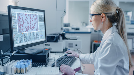 Female Scientist Sits at His Workplace in Laboratory, Uses Personal Computer. Screen Shows Analyze of DNA. I the Background Genetics Research Centre with Innovative Equipment.