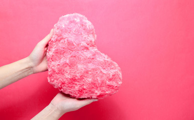 Female Hand holding plush heart on a pink background. Valentine's Day. Top view, minimalism.