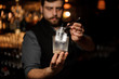 © fesenko - Bartender holding in hand an ice cube in tweezers putting it on the a cold matte cocktail glass
