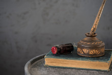 Desk With Vintage Glass And Wooden Ink Pot And Pen, On Old Book, Against Grey Background. Space For Text