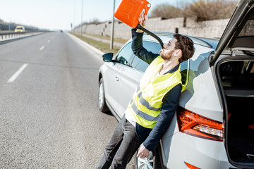 Funny portrait of a man drinking from the refuel can near the broken car on the roadside