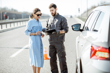 Road assistance worker signing some documents with woman near the broken car on the highway