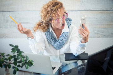 Stressed business woman shout at the phone call - two laptop on the desk and technology everywhere to work - workstation with female people - modern job and stress concept