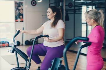 Wall Mural - Fat female practicing on stationary bike in fitness club