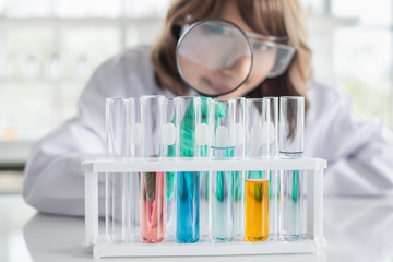 Wall Mural - a young asian woman scientist working in laboratory holding magnifying glass with test tubes and sol