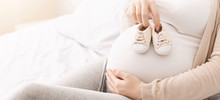 Small Shoes For Unborn Baby On Belly Of Pregnant Woman