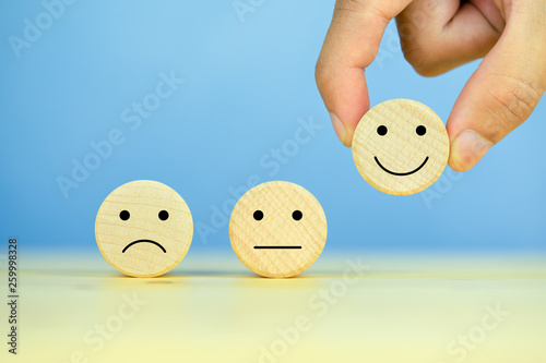 Customer service evaluation and satisfaction survey concepts. The client\'s hand picked the happy face smile face icon on wooden cube on table, blue background