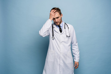 Doctor young man, medical professional terrified and nervous expressing anxiety and panic gesture, isolated over blue background.