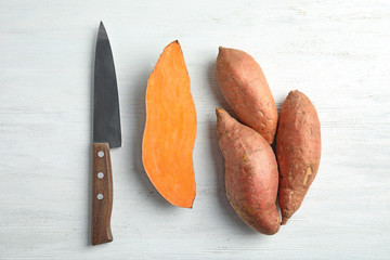 Flat lay composition with sweet potatoes and knife on white wooden background