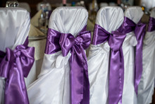 Decorated Chairs With Black Fabric And Big Pink Satin Bows. Silk Bow Tied On Back Of Chair In Party At Restaurant. Dark Cloth Cover Chairs Standing In A Row