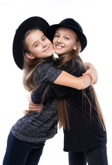 Two cute teenage girlfriends schoolgirls wearing turtleneck sweaters, jeans and hats, smiling hug each other. Isolated on white. Fashion and advertising design.