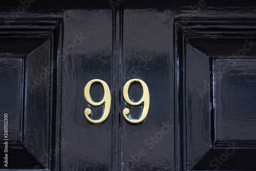 House number 99 with the ninety-nine in bronze on a black painted wooden door Poster Mural XXL