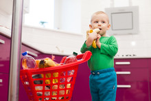 Little Boy Eats A Banana. Cheerful Little Boy With Shopping Cart. Little Kid In Casual Wear Carrying Child Plastic Shopping Trolley.