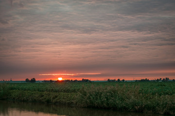 Wall Mural - the sun sets over the dutch countryside and shines on the underside of a cloud layer