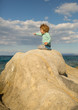 © Tverdokhlib - Adventure at sea. Sunshine smile of a child. Boy sits on a stone, warm seascape. Joyful boy playing on beach. Happiness and Nature. Happy childhood with outdoor games. A child is enjoying fun game.