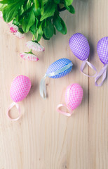 Wall Mural - Top view of pastel pink and blue checkered Easter eggs decorations and blooming pink and white daisies on pale wooden background. Easter eggs and spring flowers background