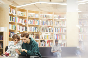 Wall Mural - Serious concentrated young students in casual clothing sitting in modern library area and using tablet while searching for useful information together