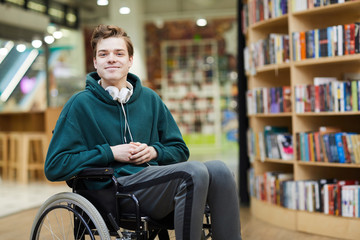 content handsome young disabled student with headphones on neck siting in wheelchair and looking at 