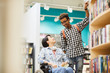 © Seventyfour - Cheerful handsome black guy with Afro hairstyle helping disabled student girl to take book from shelf in library