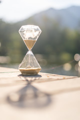 Hourglass clock on white wooden table with bokeh sunset light of lake abstract background.