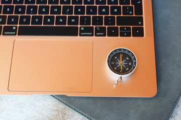 Rose-gold laptop keyboard and compass. Internet navigation or travel and online booking concept.