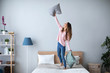 © BestForYou - Young cheerful woman having fun with pillows on the bed at home.