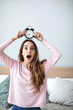© BestForYou - Anxious woman with an alarm clock on her head at home.