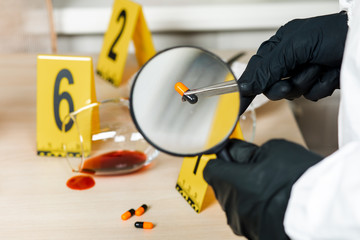 A policeman looks through a magnifying glass at the evidence at the crime scene. The crime scene of poisoning and overdosing