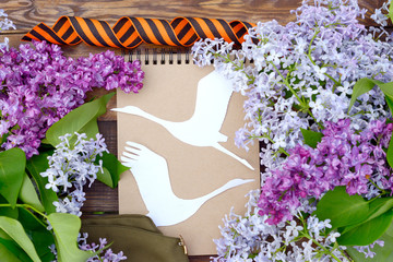 Wall Mural - May 9 victory Day. Branches of blooming lilac for viewing, military cap, St. George's ribbon and a white paper crane on a wooden background / Cranes-the memory of the dead soldiers.Concept of memory.