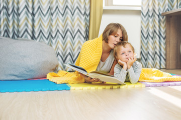 Happy and beautiful mother and child, family together reading a book lying in the nursery under the covers