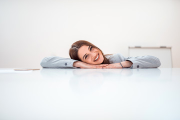 Wall Mural - Smiling brunette businesswoman lying on a table and looking at camera, copy space.