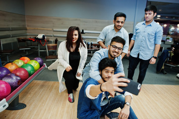 Group of five south asian peoples having rest and fun at bowling club. Making selfie by phone.