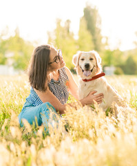 Wall Mural - Pretty brunette woman playing with a dog white golden retriever on the grass in park. Woman with her dog on green meadow, puppy training