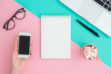 Wall Mural - Top view flatlay blank notepad with notebook, glasses and holding phone at pink and mint background desktop