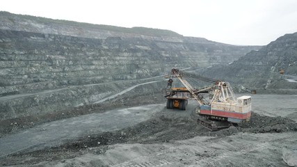 Wall Mural - Excavator fills dump truck with earth in open pit. Heavy machinery works in mining industry in open pit