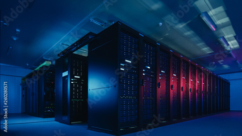 Shot of Data Center With Multiple Rows of Fully Operational Server Racks. Modern Telecommunications, Cloud Computing, Artificial Intelligence, Database. Shot in Dark with Neon Blue, Pink Lights.