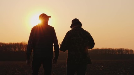 Wall Mural - Farmers father and son walk across the field at sunset, chatting