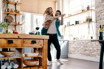 Poster - Playful. Full length of beautiful young couple in casual clothing dancing and smiling while standing in the kitchen at home