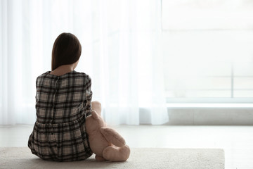 Wall Mural - Upset girl with toy sitting near window indoors. Space for text