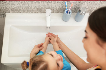 Wall Mural - Mother and daughter washing hands in bathroom at home, above view