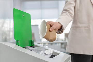 Wall Mural - Woman putting used paper cup into trash bin in modern office, closeup. Waste recycling