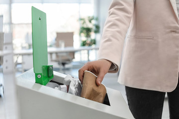 Wall Mural - Woman putting used paper cup into trash bin in modern office, closeup. Waste recycling