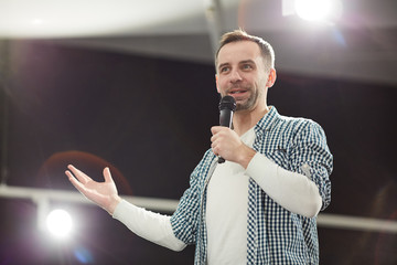 waist up portrait of mature man giving speech standing on stage in spotlight and speaking to microph