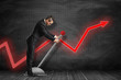 © gearstd - Side view of businessman looking down and pulling big lever near black graph ruled wall with red graph arrow on it.